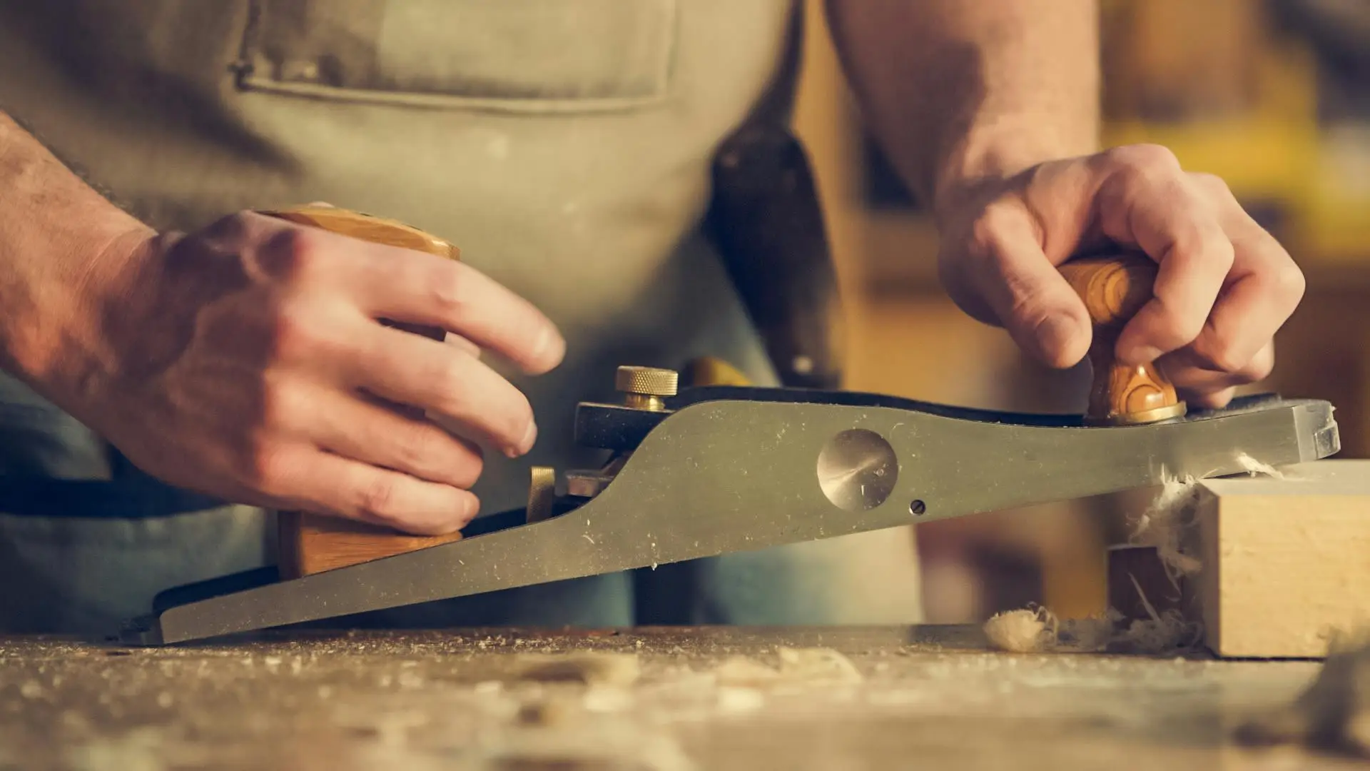 A carpenter skillfully using a hand plane on a wooden surface indoors.